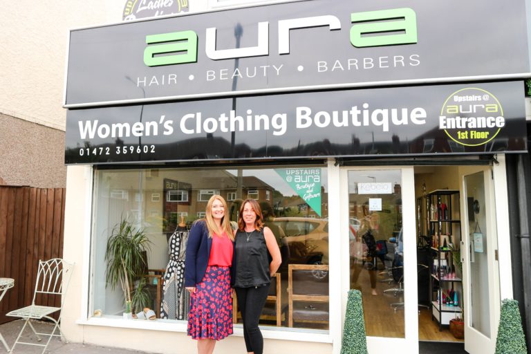 Two women standing in front of women's clothing boutique Aura.